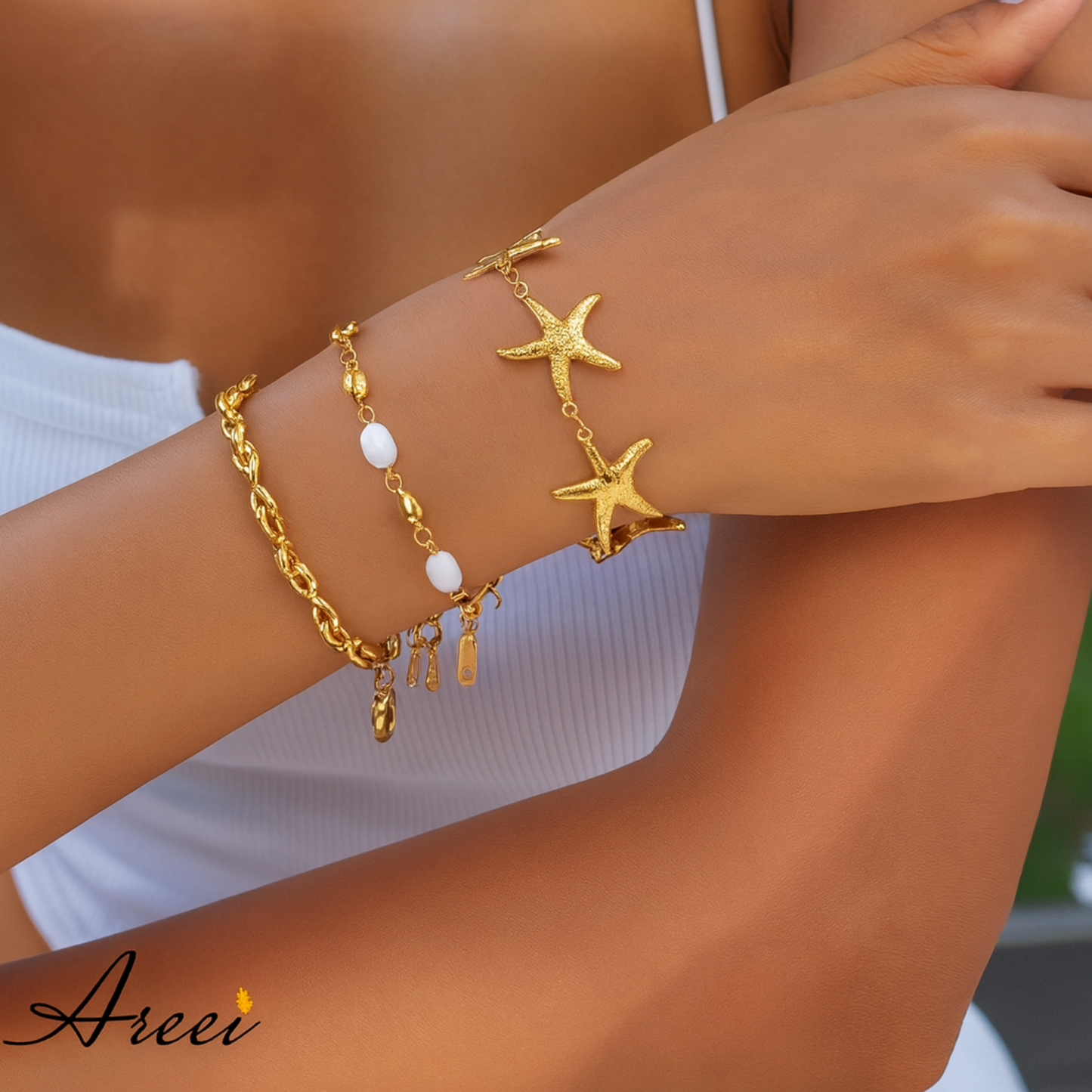Gold bracelet with starfish and pearl charms on a wrist, brand 'Areei' visible.