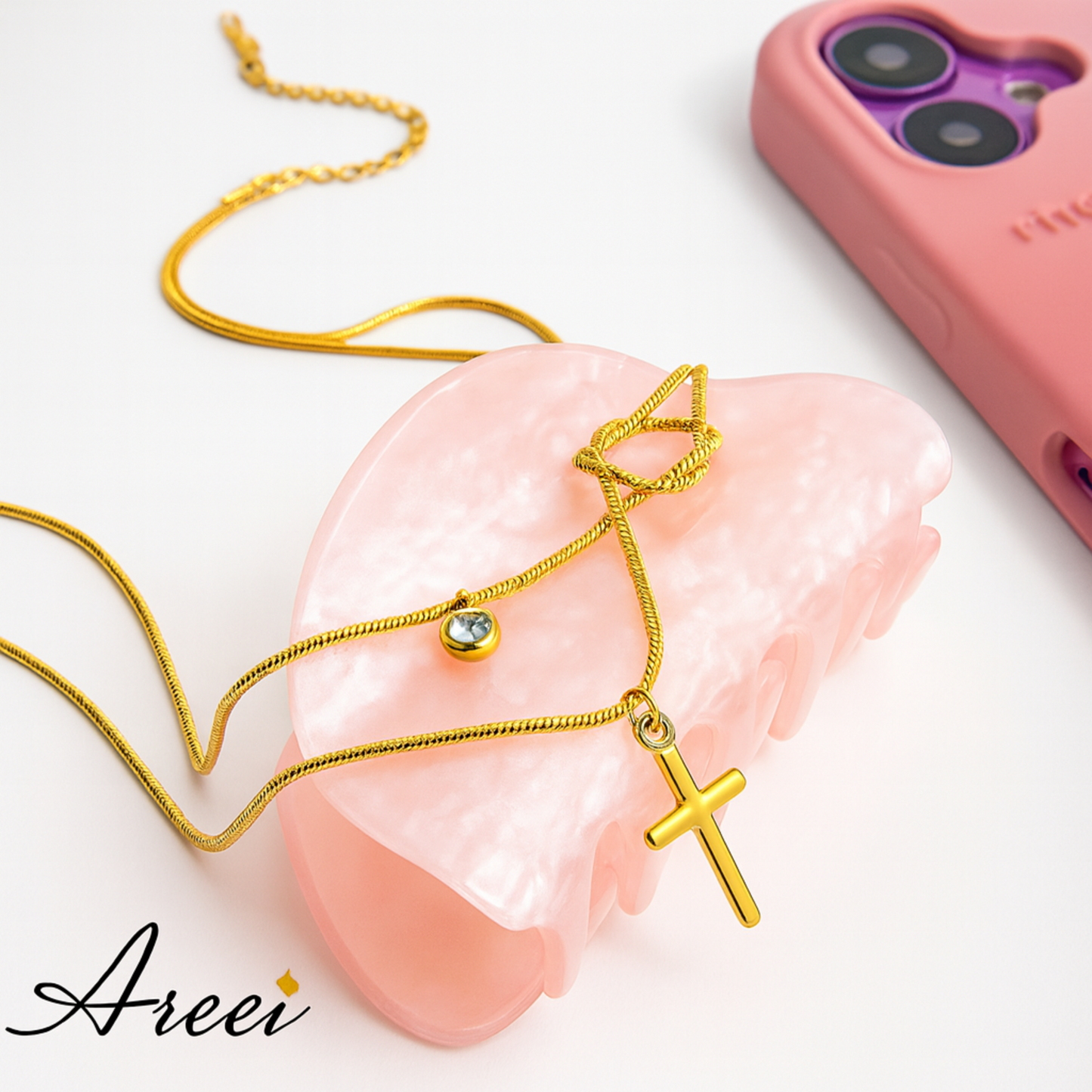 Gold necklace with a cross pendant on a pink stone, with 'Areei' branding.