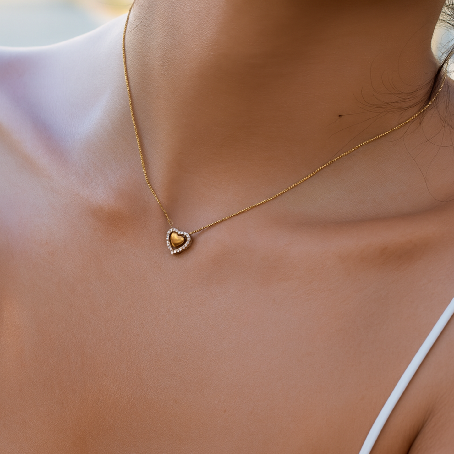 Gold heart-shaped necklace on a person's neck with a blurred background