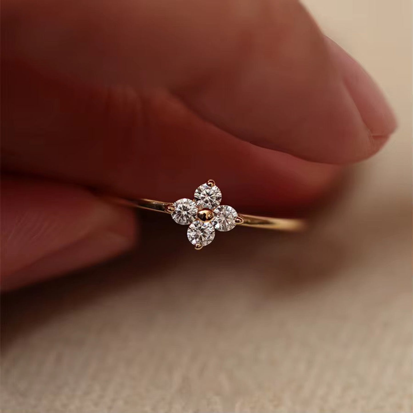 Rose gold ring with diamond accents held between fingers on a beige background