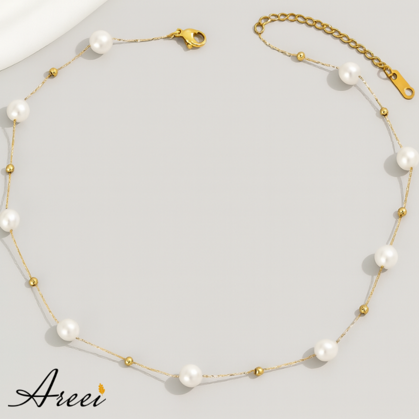 Pearl necklace with gold accents on a light gray background, featuring the brand 'Areei'.