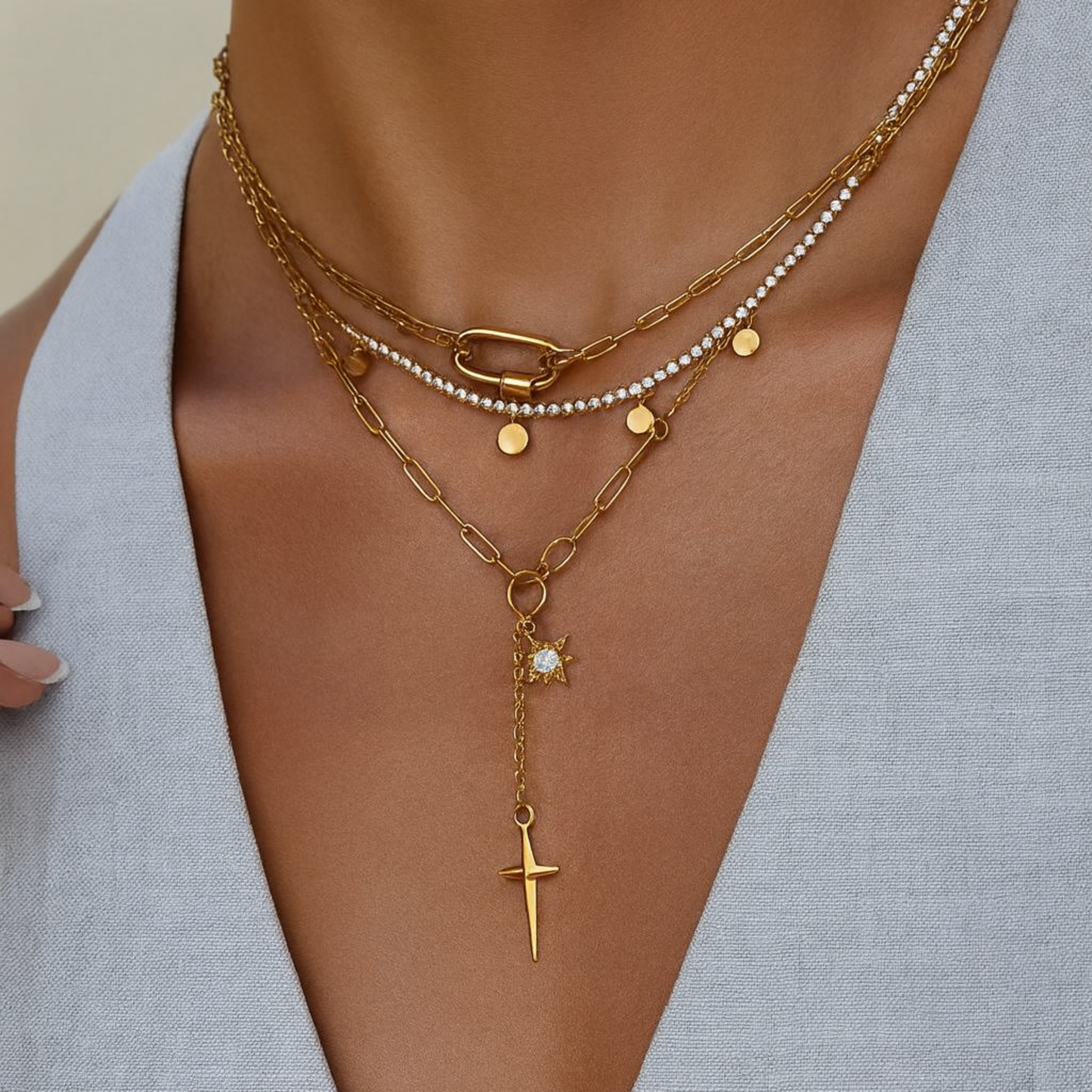 Layered gold necklaces with a star and cross pendant on a neutral background