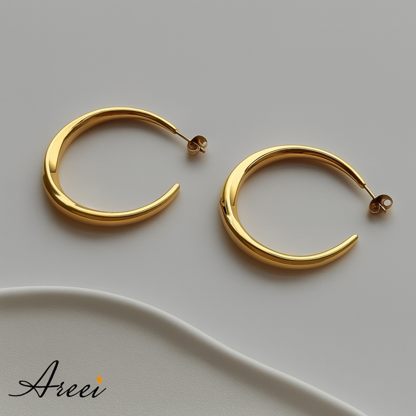 Gold hoop earrings on a light gray background with 'Areei' branding.