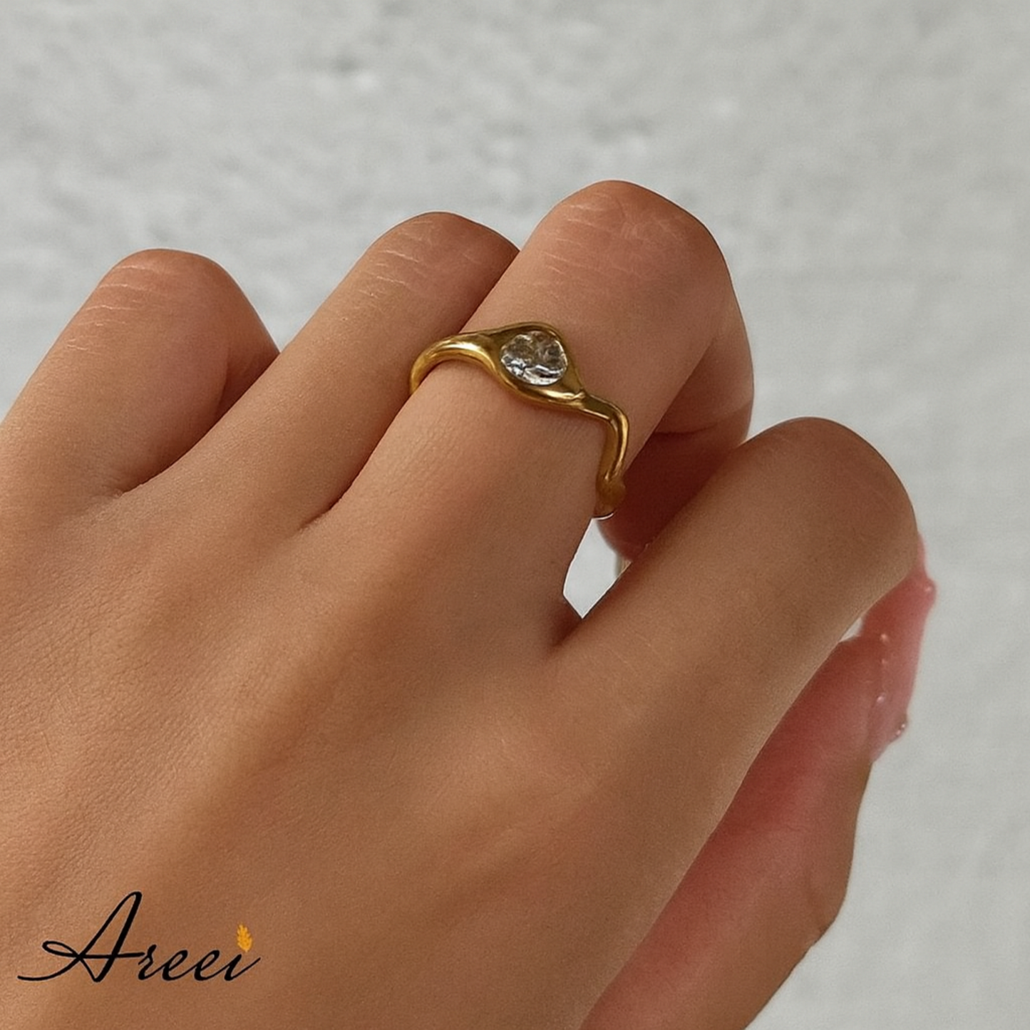 Gold ring with a diamond on a hand, brand 'Areei' visible