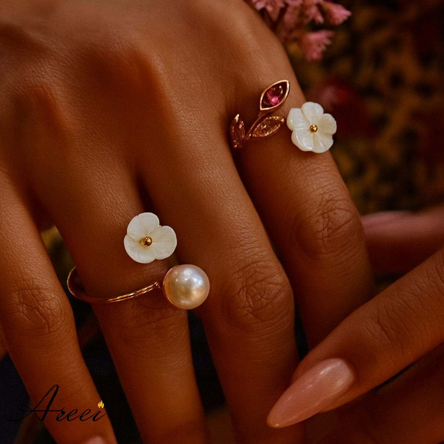 Close-up of a hand wearing two rings with floral and pearl designs, with 'Areei' branding.
