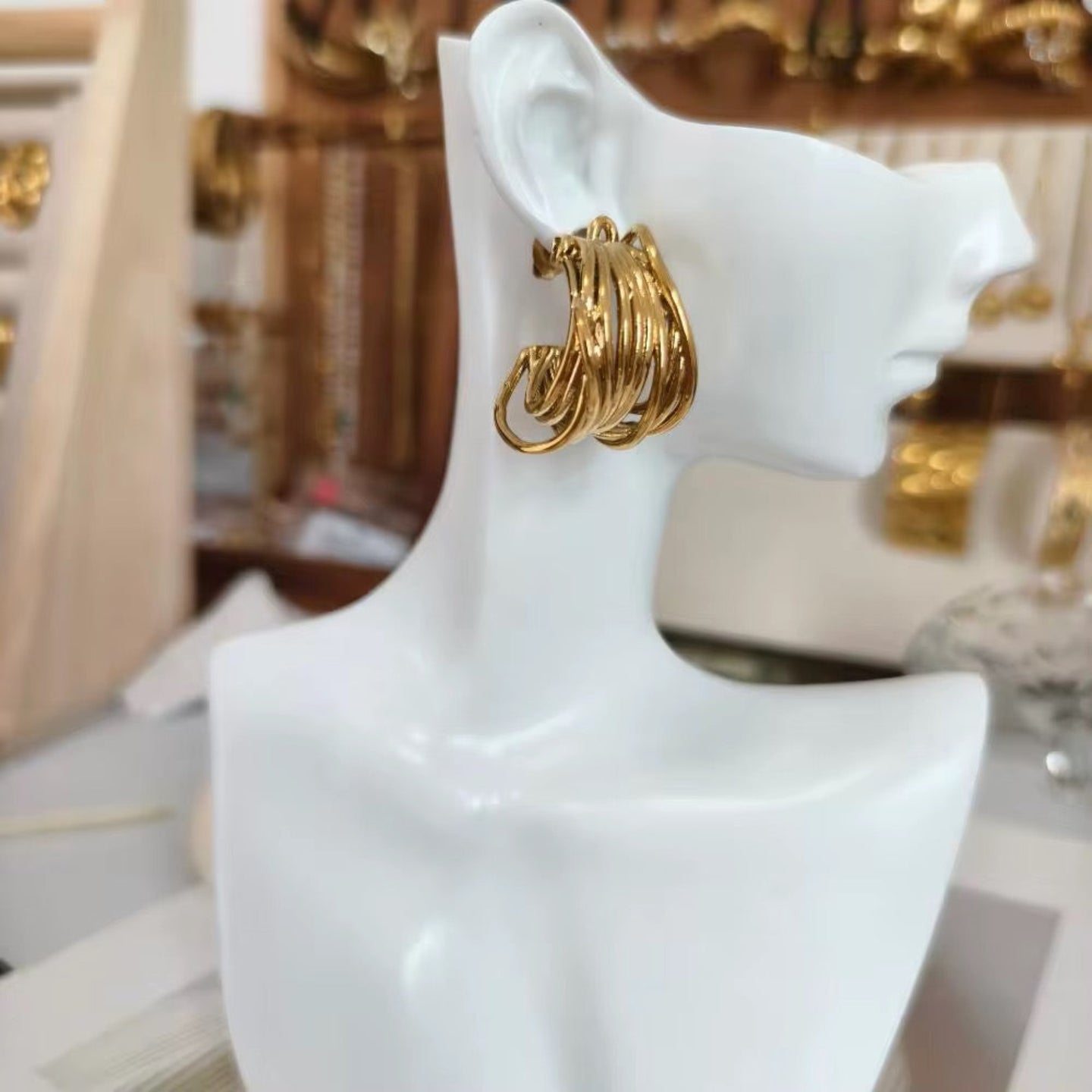 Gold hoop earrings on a white mannequin bust with a blurred background