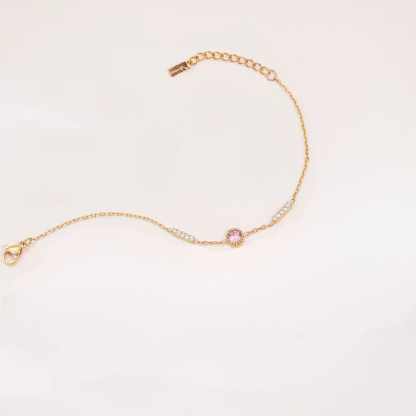 Gold bracelet with a pink gemstone on a light beige background