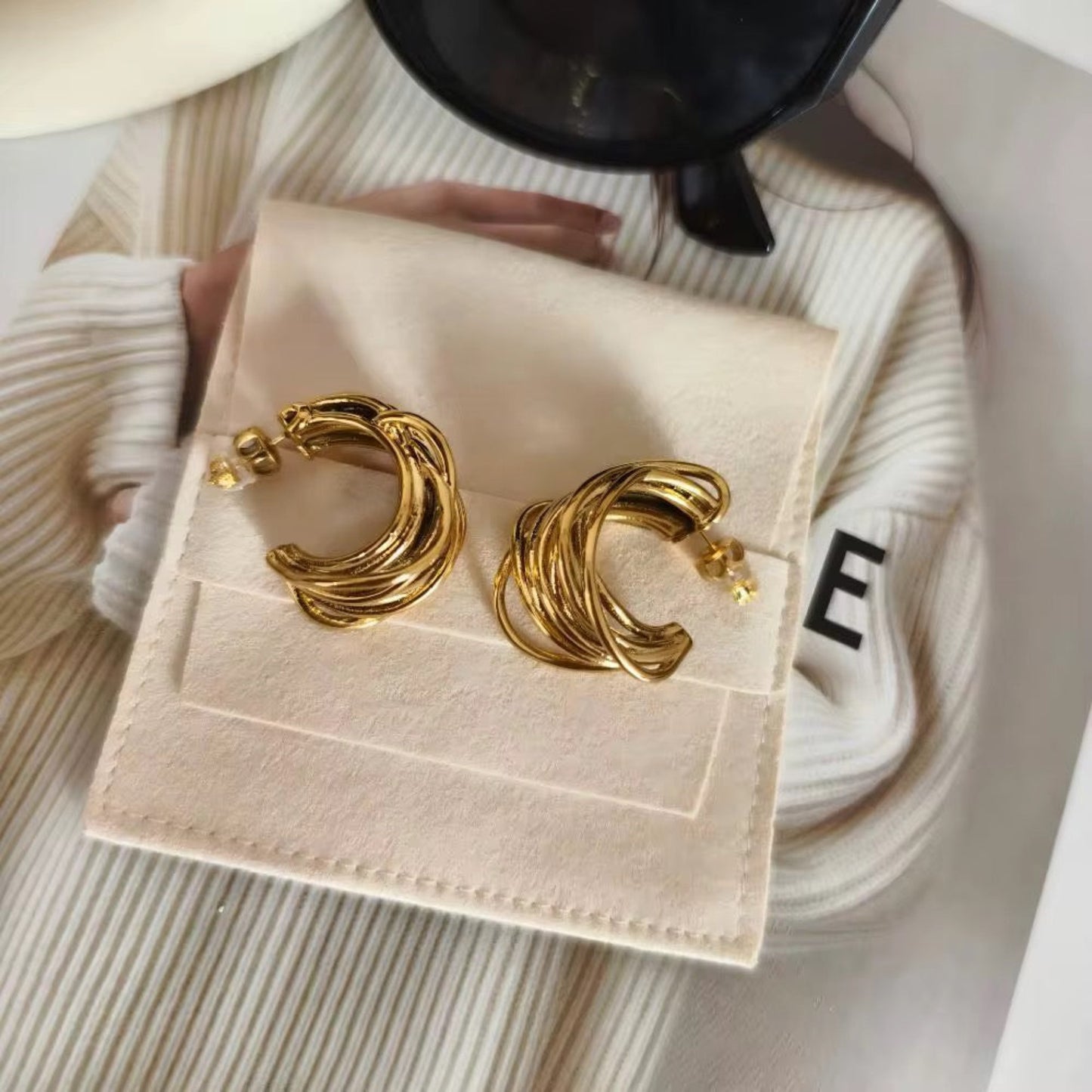 Gold hoop earrings on a beige jewelry display box with a blurred background.