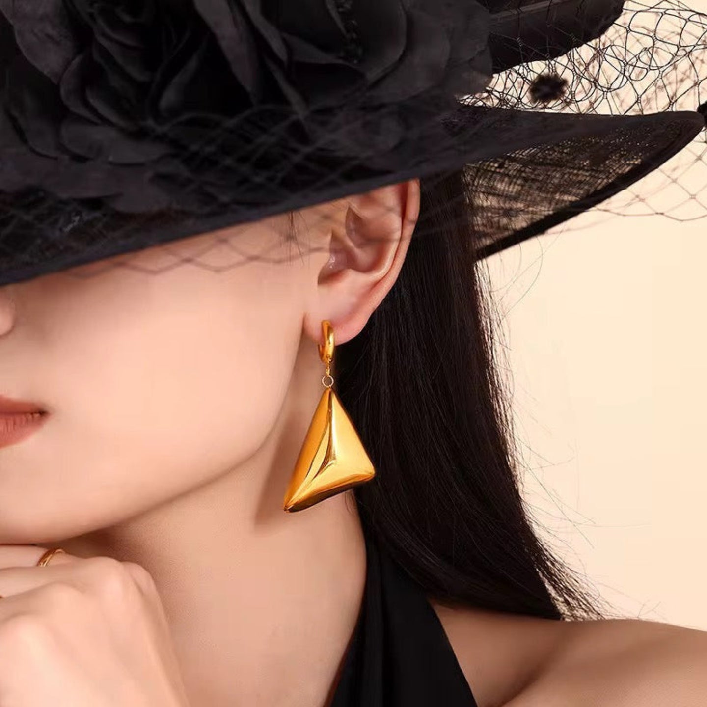 Close-up of a woman wearing a gold earring with a black hat on a beige background
