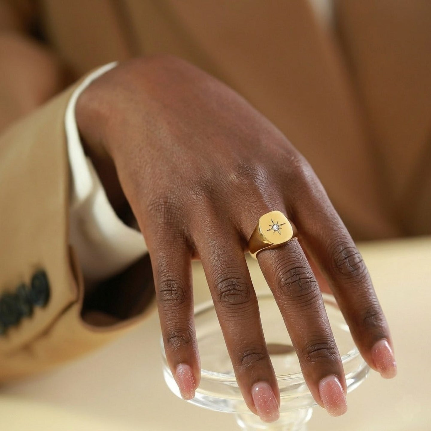 Hand wearing a gold ring with a diamond on a neutral background