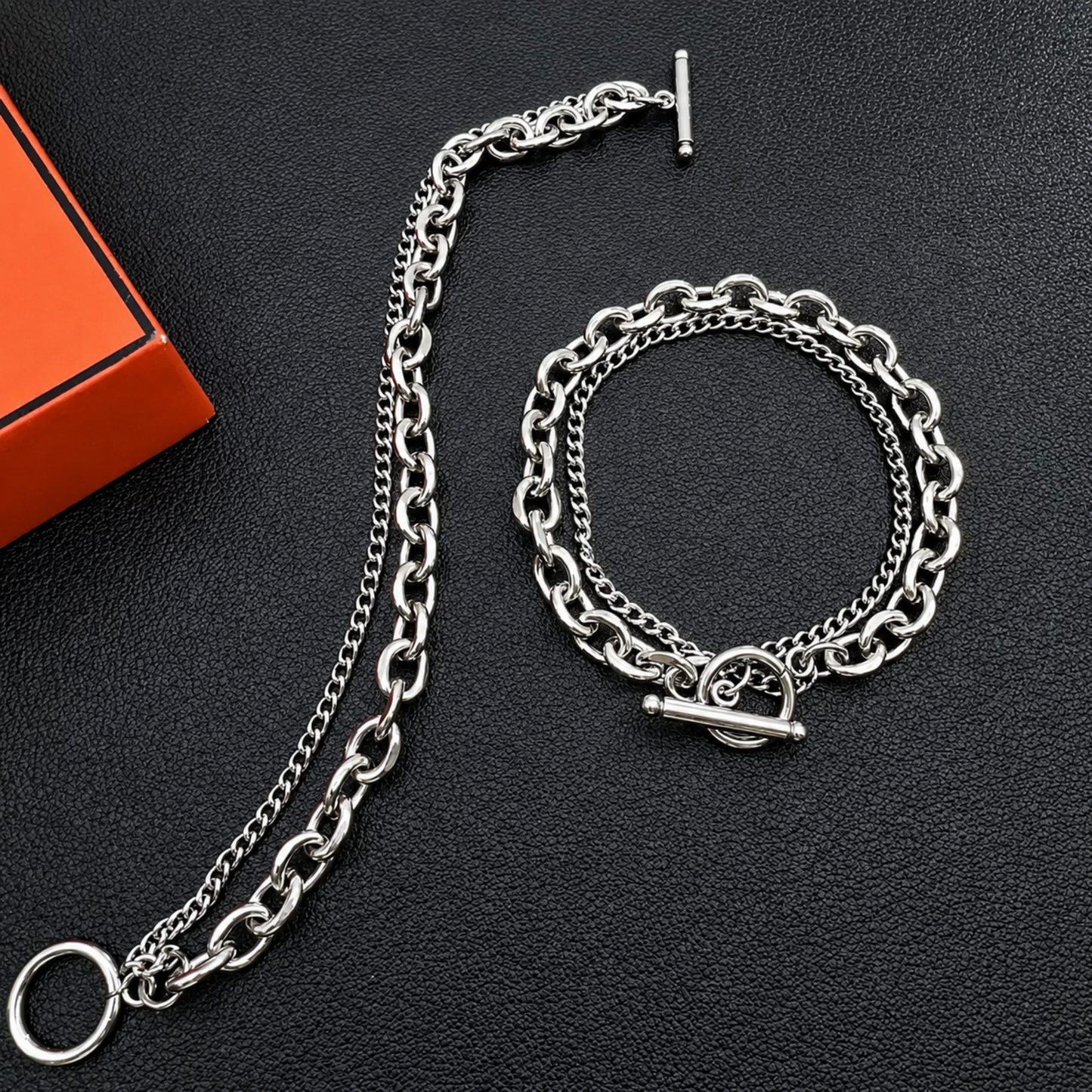 Silver chain belt and bracelet set on a dark surface with an orange box.