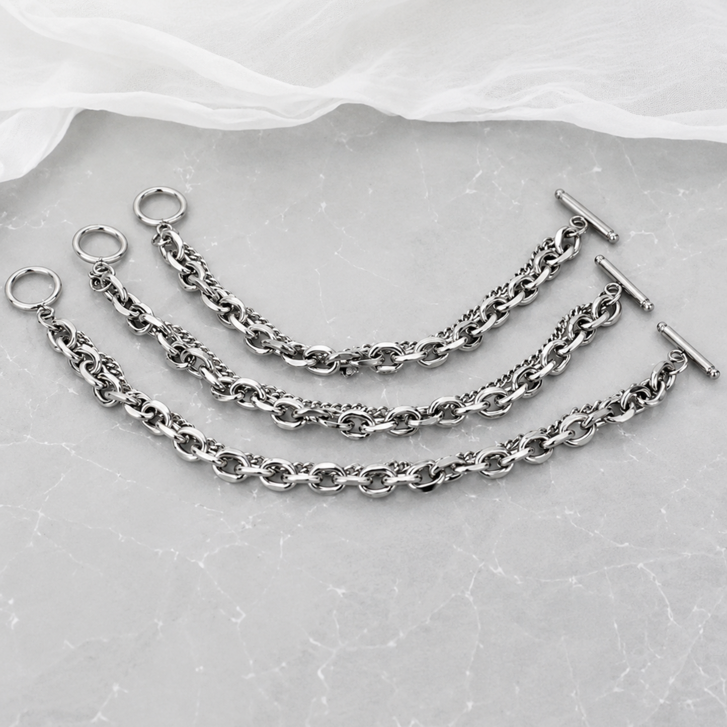 Set of silver chains with clasps on a textured gray surface