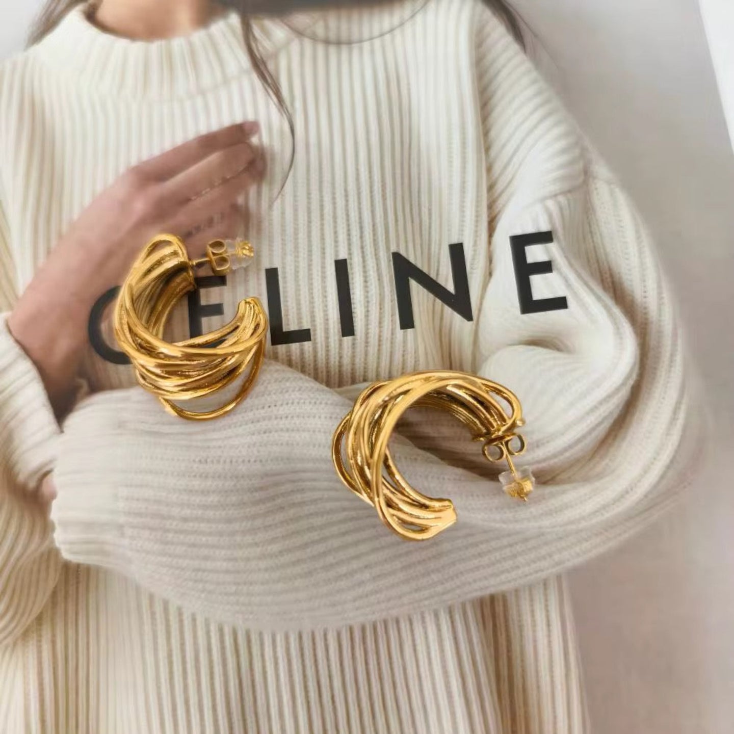 Gold earrings held by a person wearing a Celine sweater