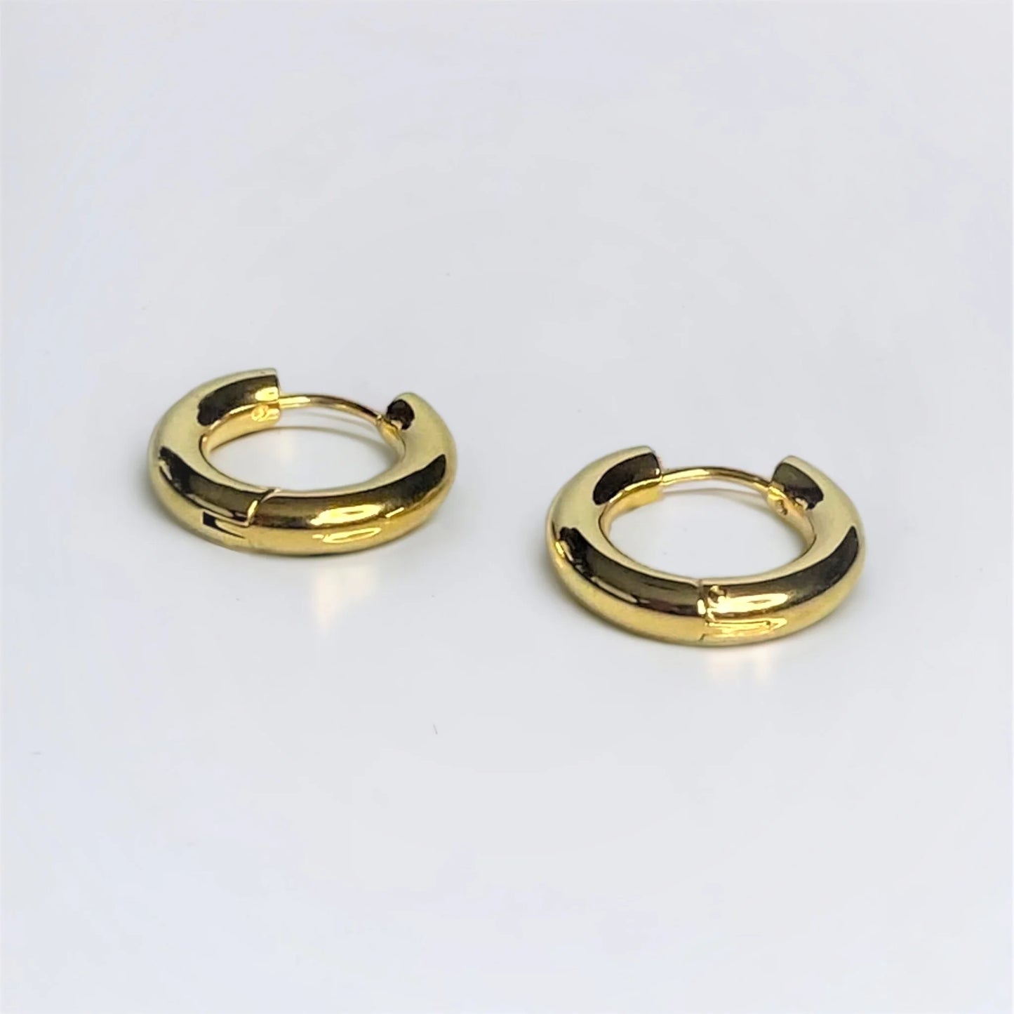 Zoomed in Chunky gold circle huggie earrings on white surface