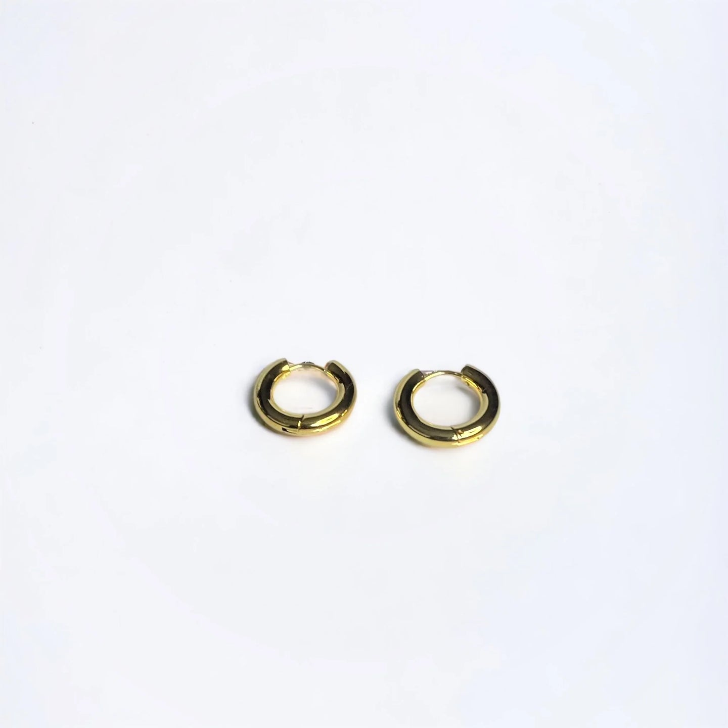 Chunky gold circle huggie earrings on white surface