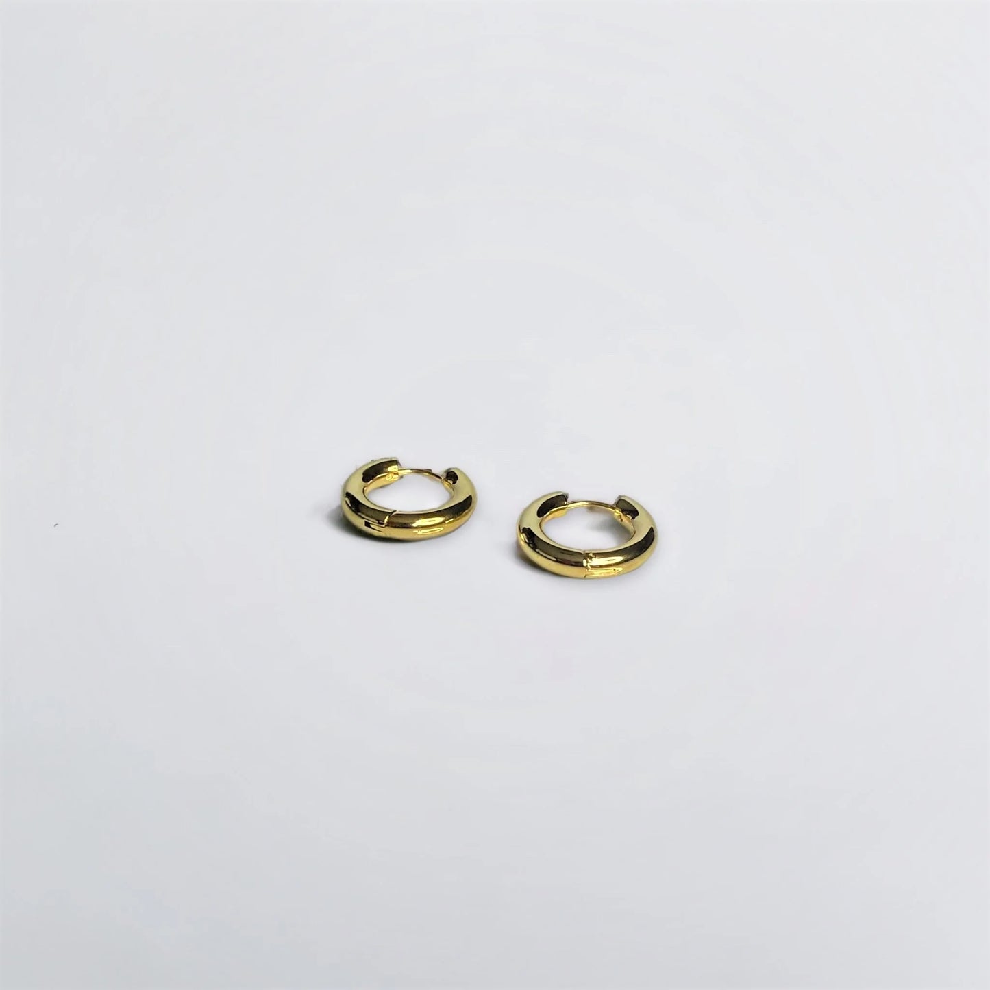 Chunky gold circle huggie earrings on white surface