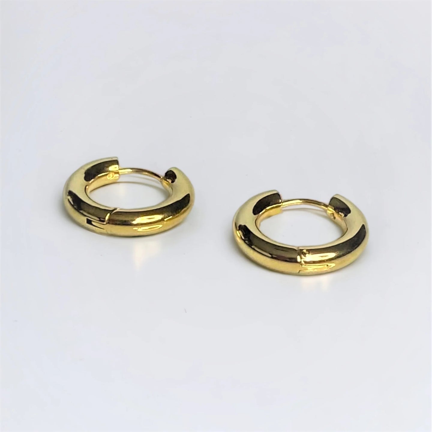 Zoomed in Chunky gold circle huggie earrings on white surface