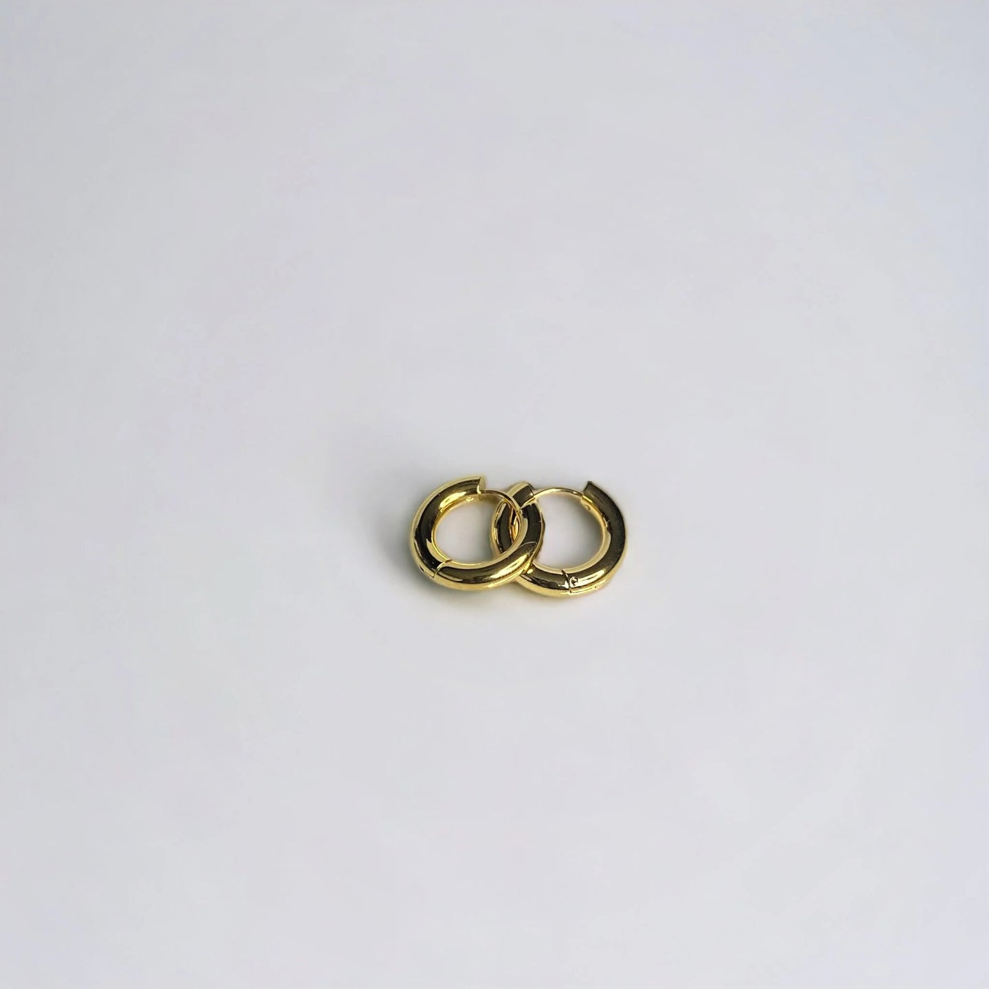 Chunky gold circle huggie earrings stacked on white surface