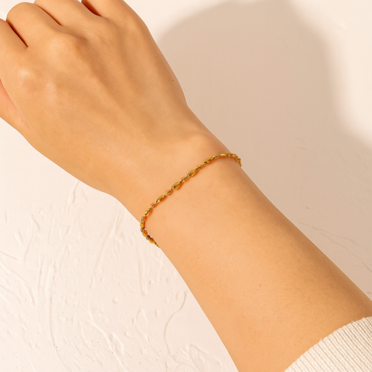 Gold bracelet on a person's wrist against a neutral background