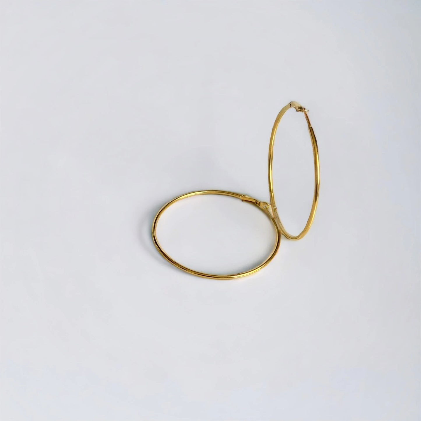 Large gold hoop earrings with one vertical on white surface