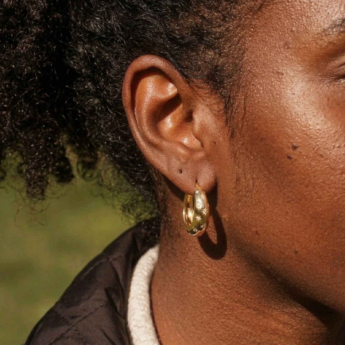 Close-up of a person wearing a gold earring with a blurred natural background