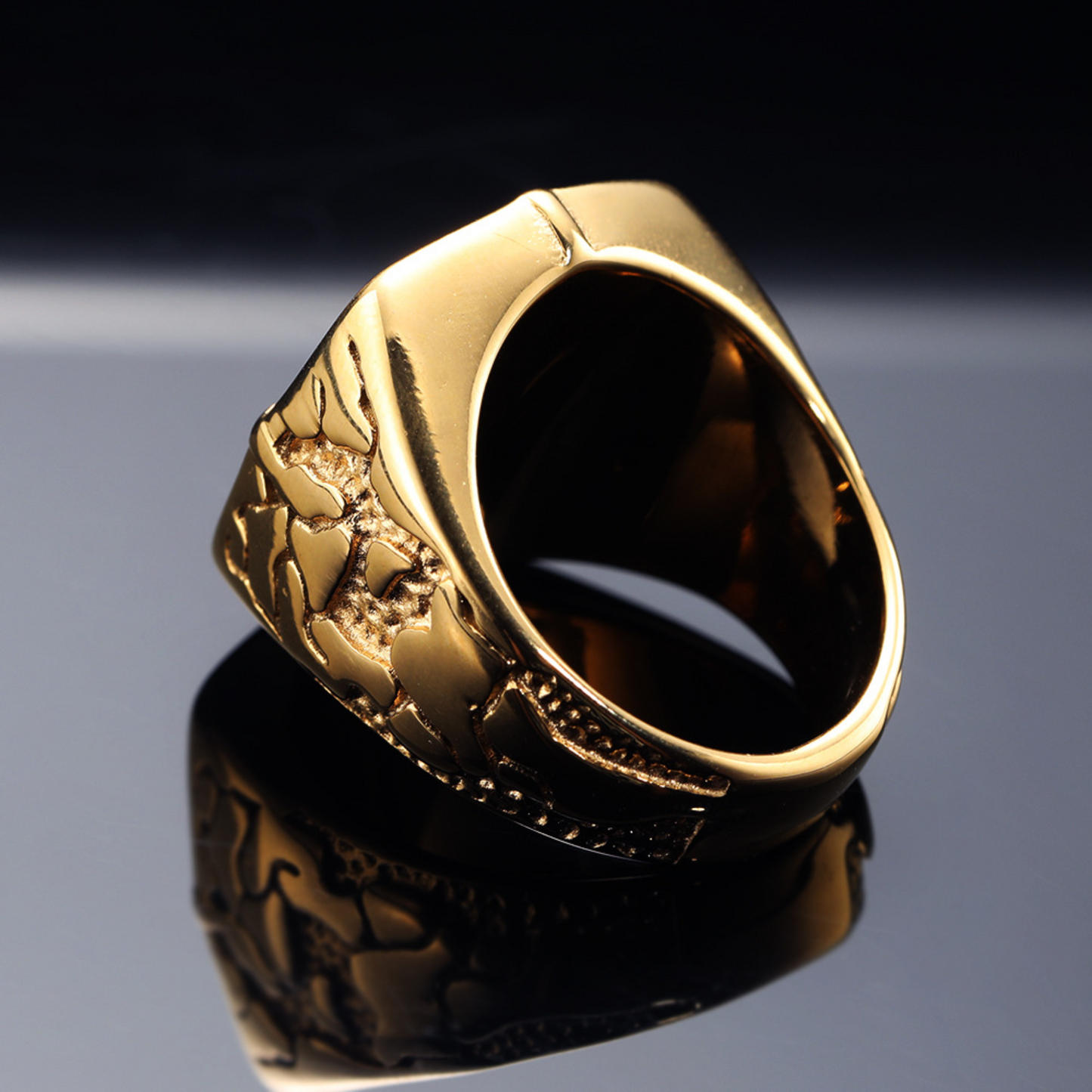 Gold ring with intricate design on a reflective surface