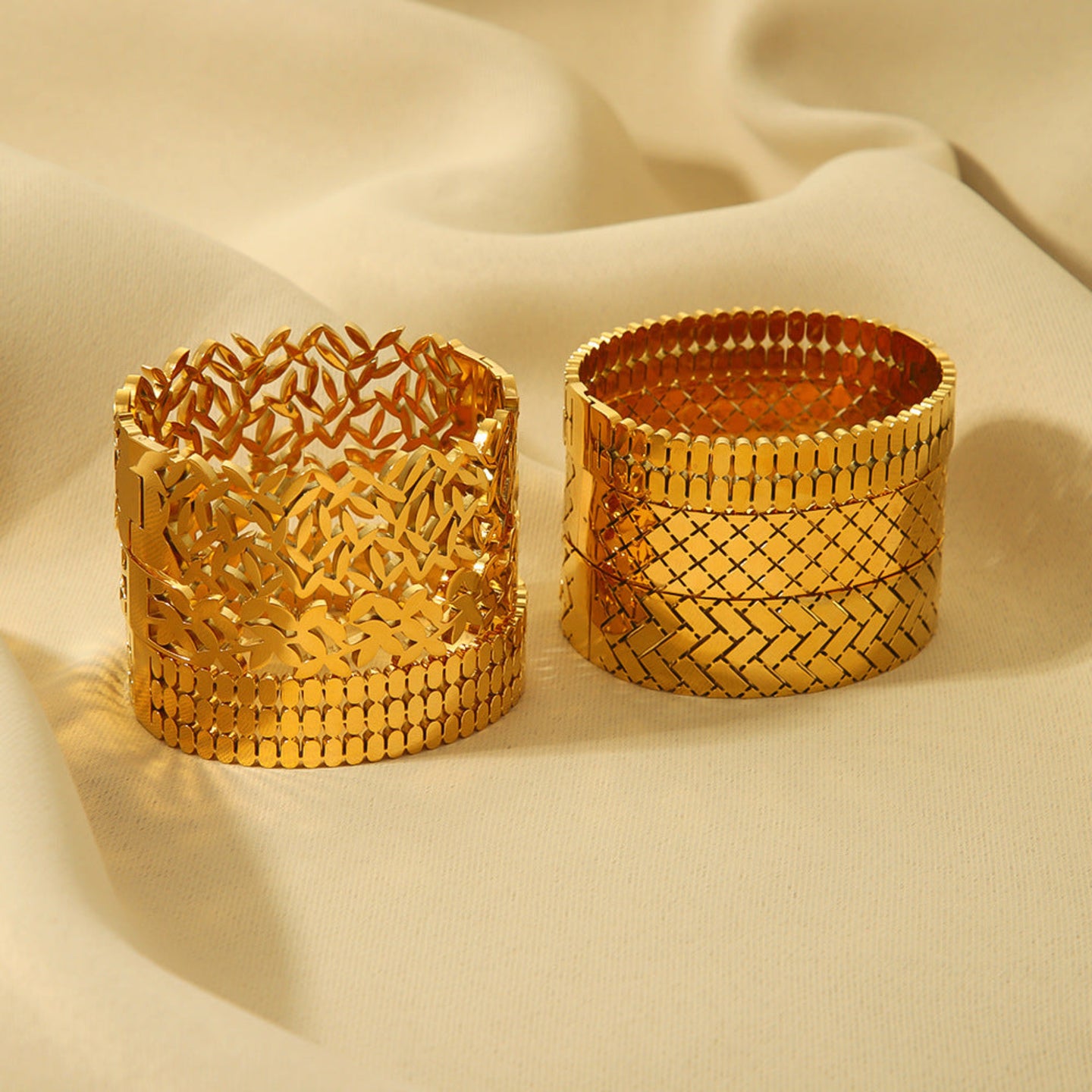 Two gold bracelets with intricate patterns on a beige fabric background
