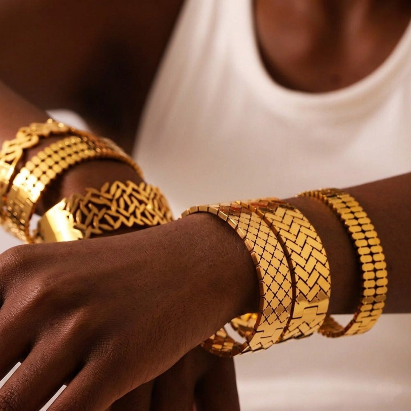 Close-up of a person's arm wearing multiple gold bracelets on a neutral background