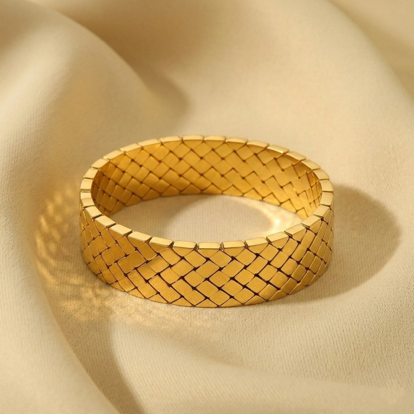 Gold woven bracelet on a beige fabric background