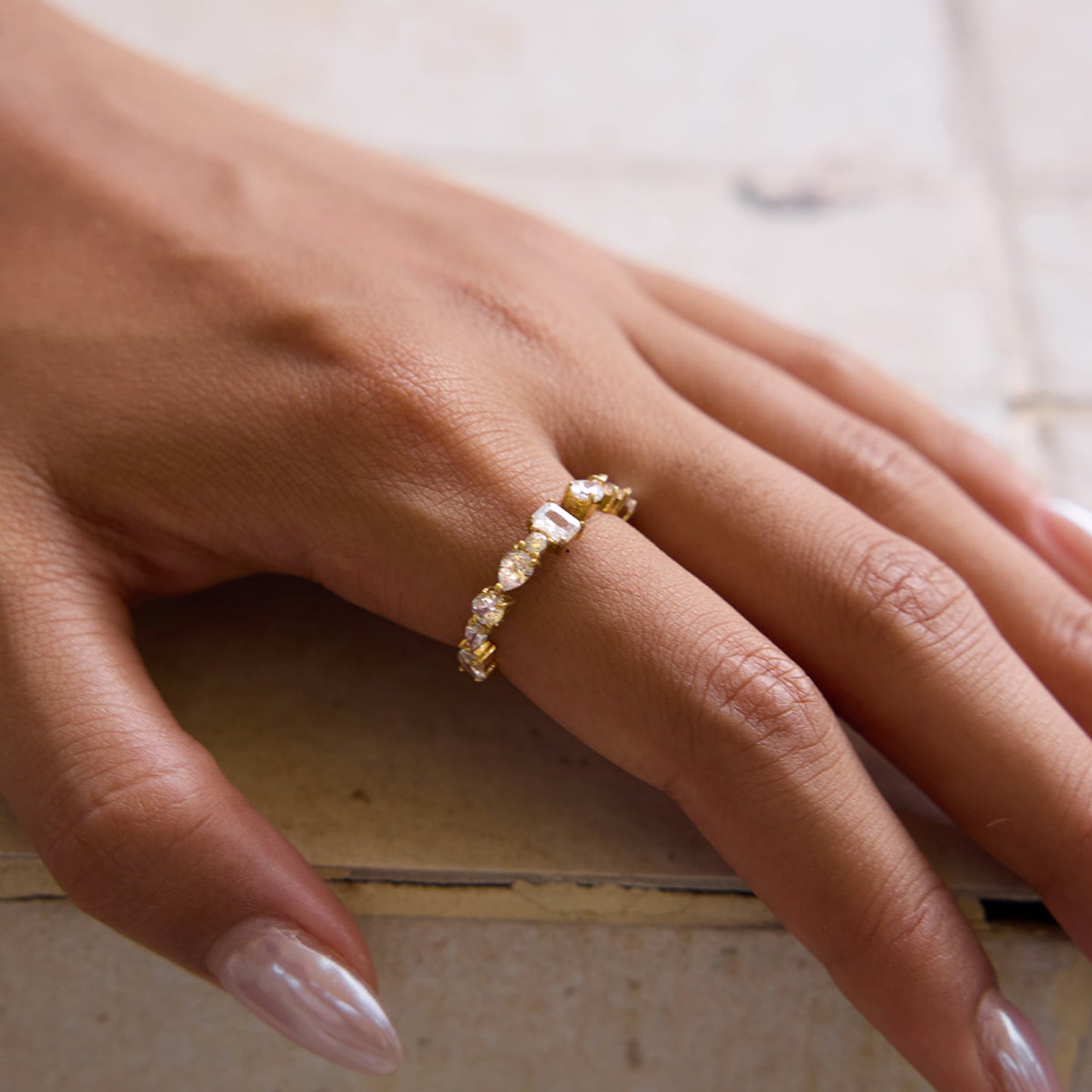 Gold ring with diamonds on a person's finger against a neutral background
