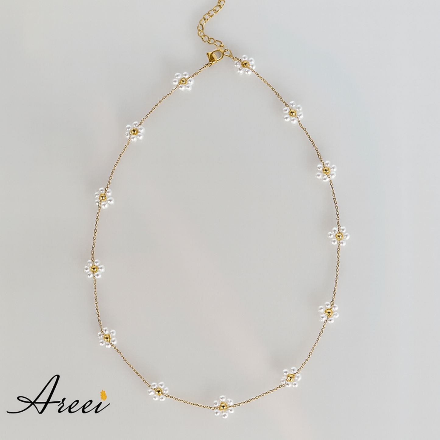 Delicate gold necklace with floral pendants on a light gray background, featuring the brand 'Areev'.