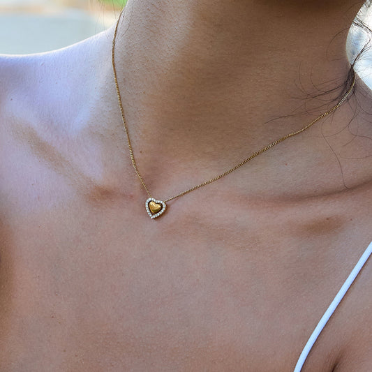 Gold heart-shaped necklace on a person's neck with a blurred background