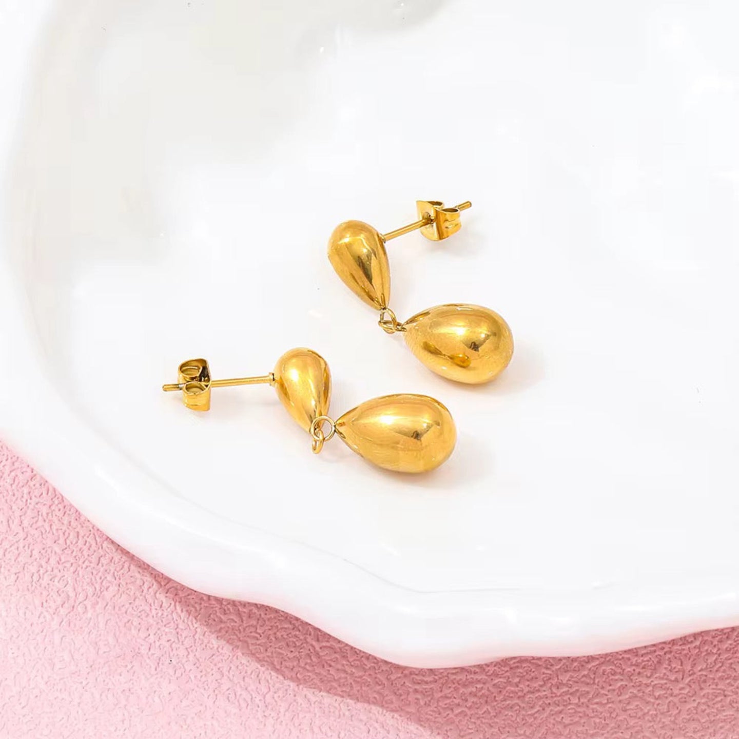 Gold teardrop earrings on a white and pink background