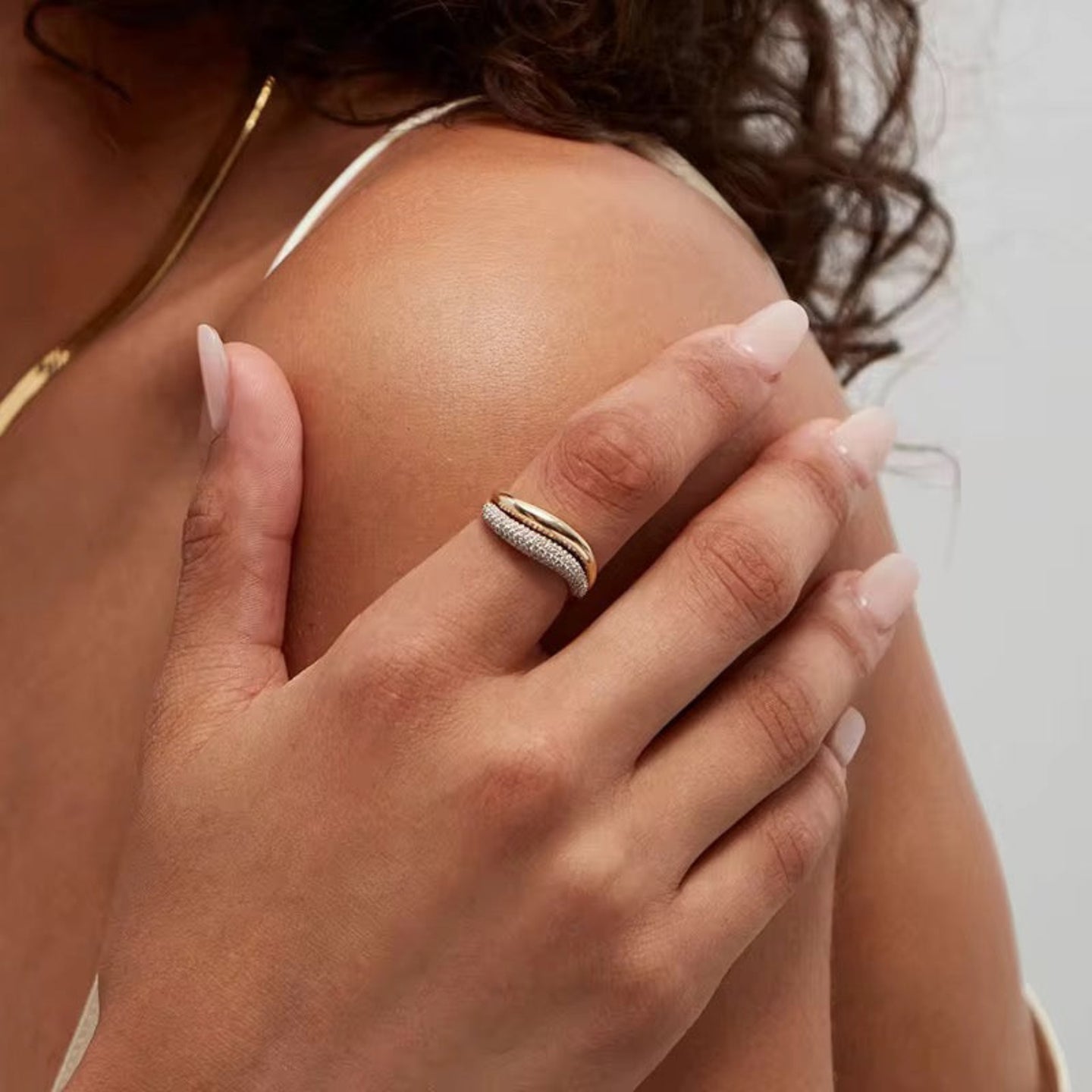 Close-up of a hand wearing a gold ring with a diamond, holding a shoulder.