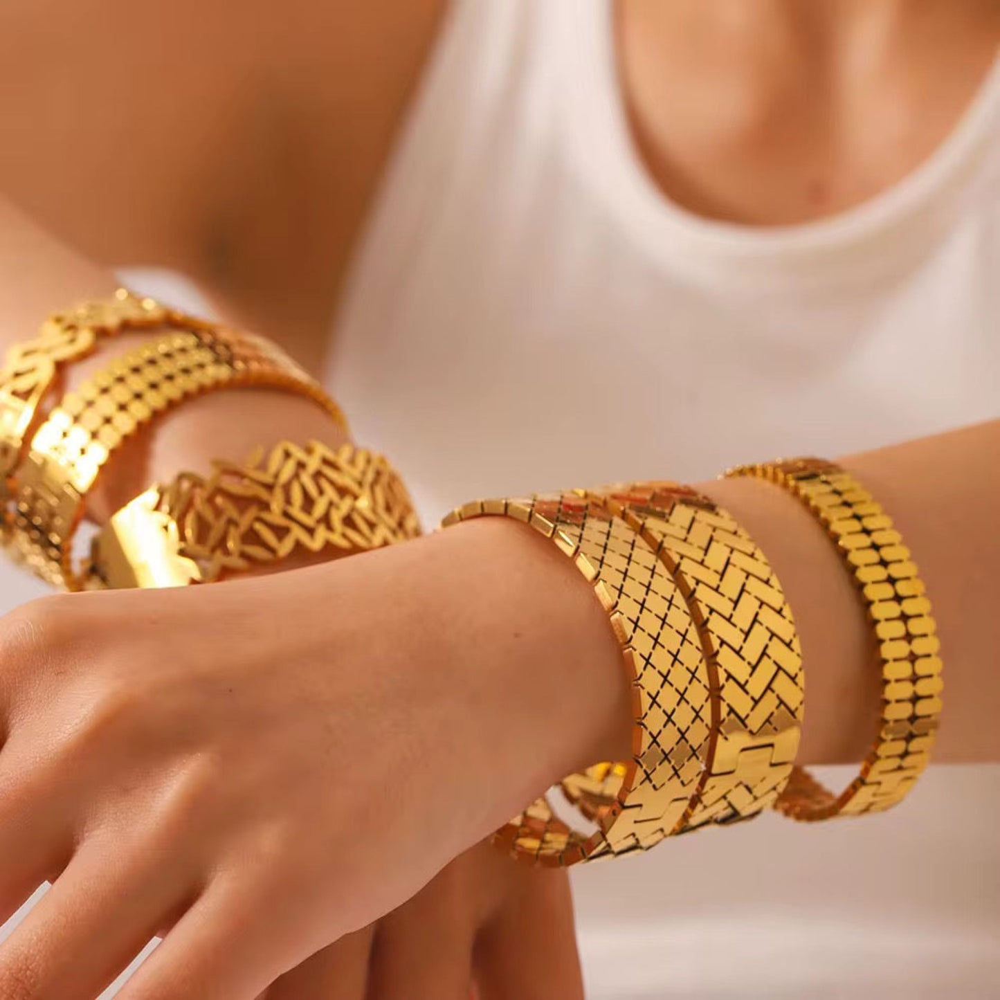 Gold bracelets on a person's wrist with a neutral background