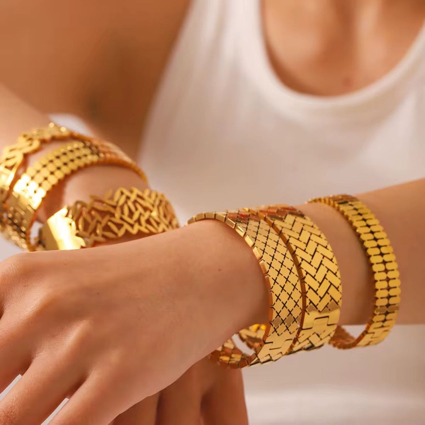 Gold bracelets on a person's wrist with a neutral background