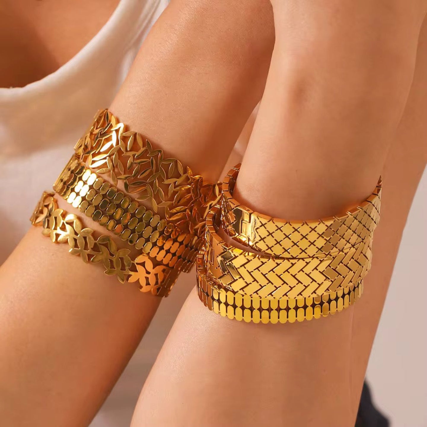 Gold metallic anklets on a person's hand against a neutral background