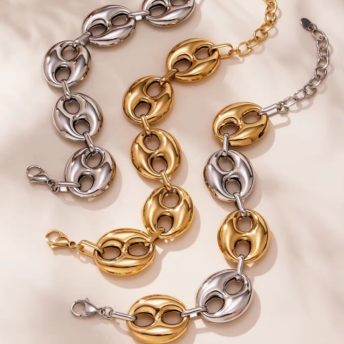 Two chain bracelets, one gold and one silver, on a light pink surface.