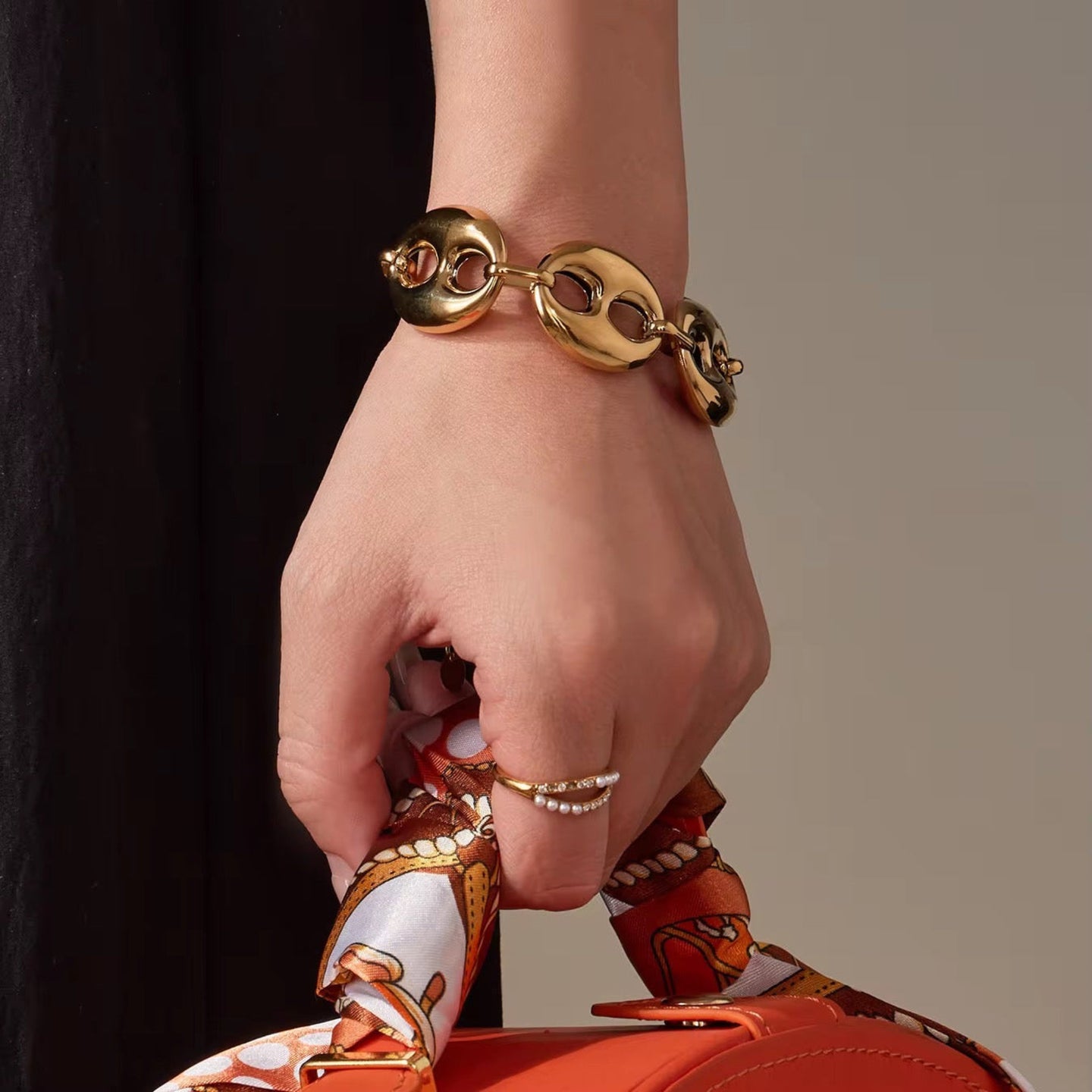 Hand wearing a gold bracelet holding an orange handbag with decorative handle.