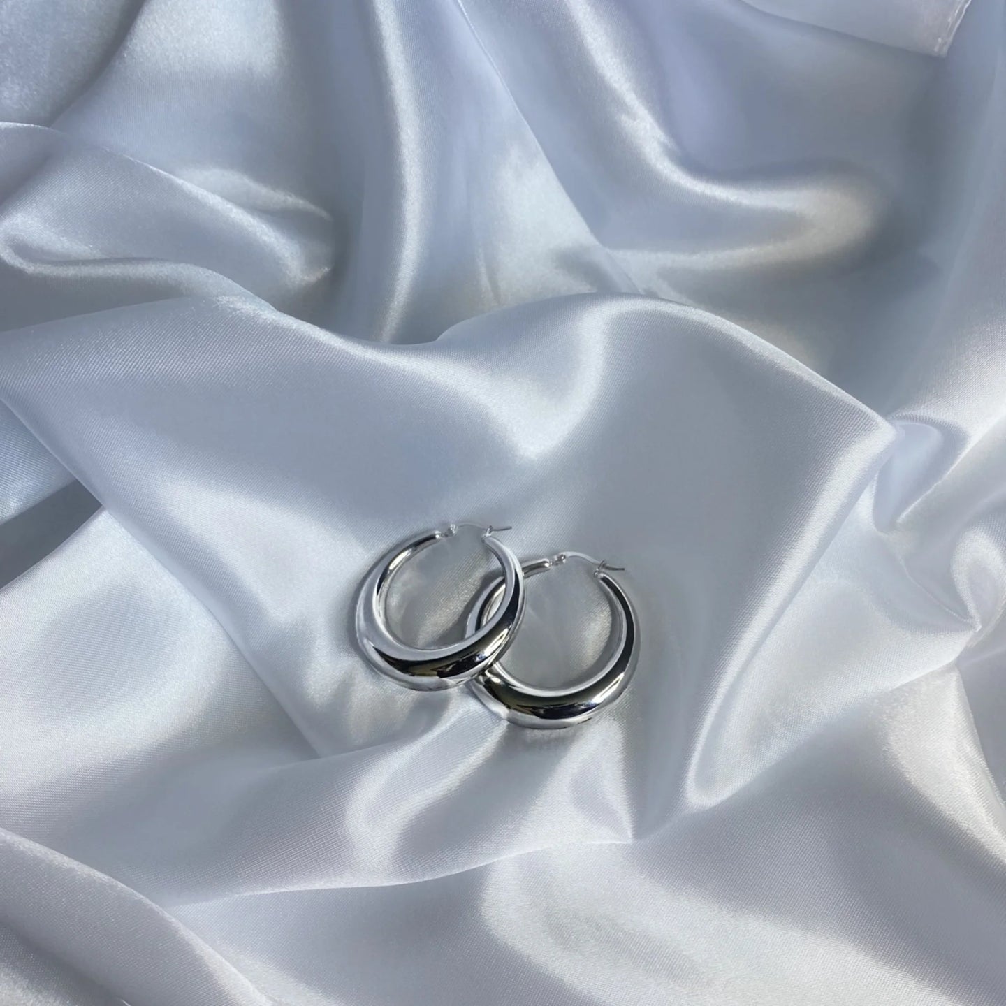 Silver chunky medium sized hoops on white silk sheet