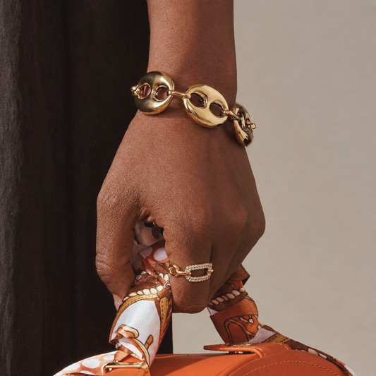 Hand wearing a gold bracelet with a neutral background