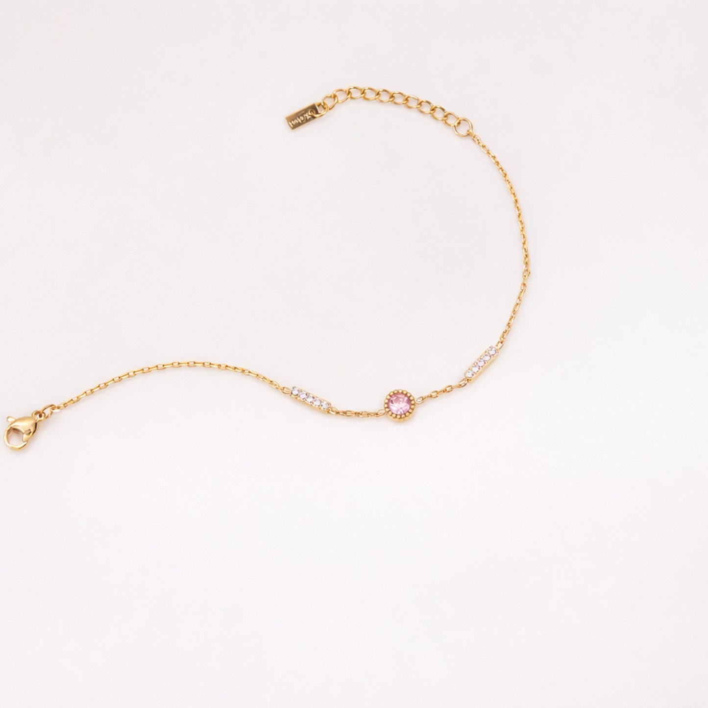 Gold bracelet with a pink gemstone on a light gray background