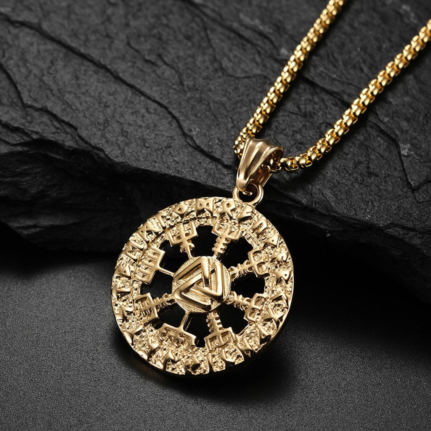 Gold necklace with a detailed pendant on a dark stone surface