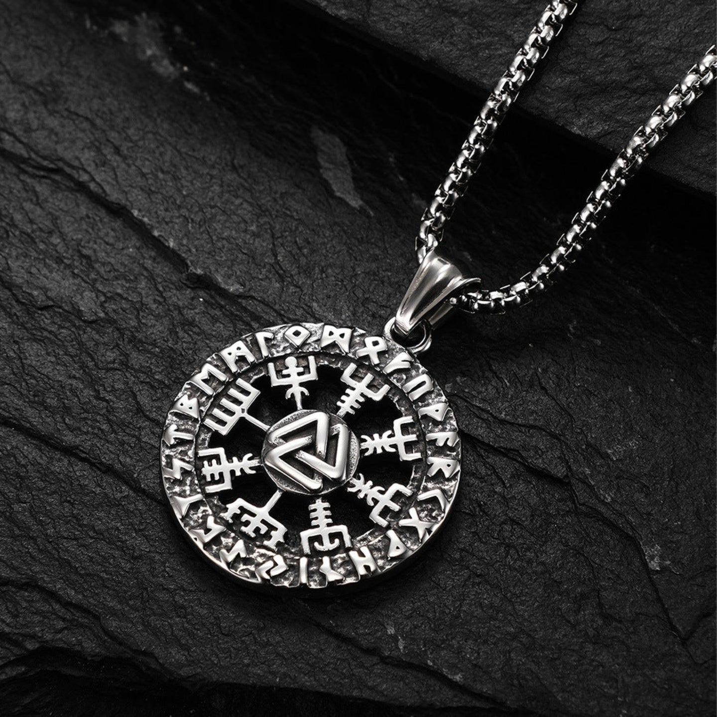 Silver pendant necklace with intricate design on a dark stone surface