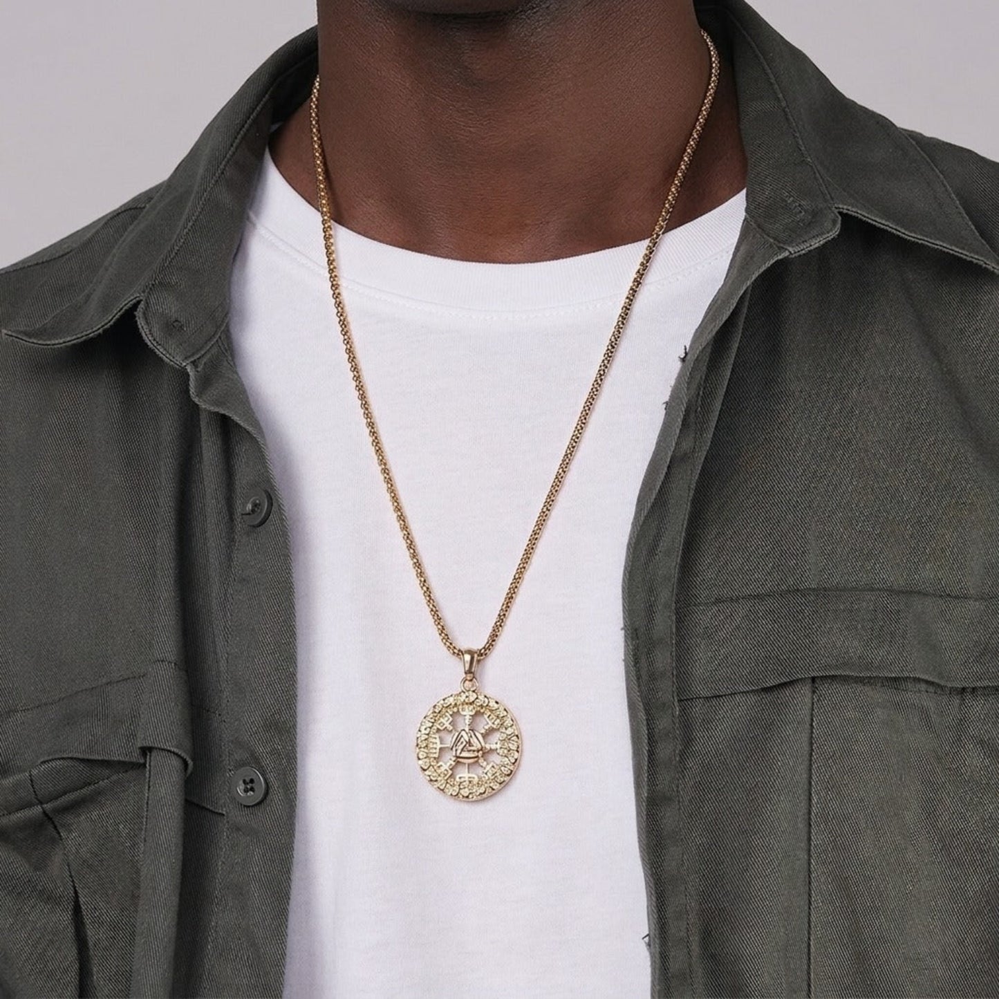 Person wearing a gold necklace with a detailed pendant on a plain background
