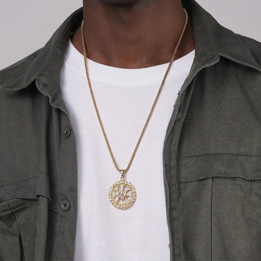 Person wearing a gold necklace with a detailed pendant on a plain background