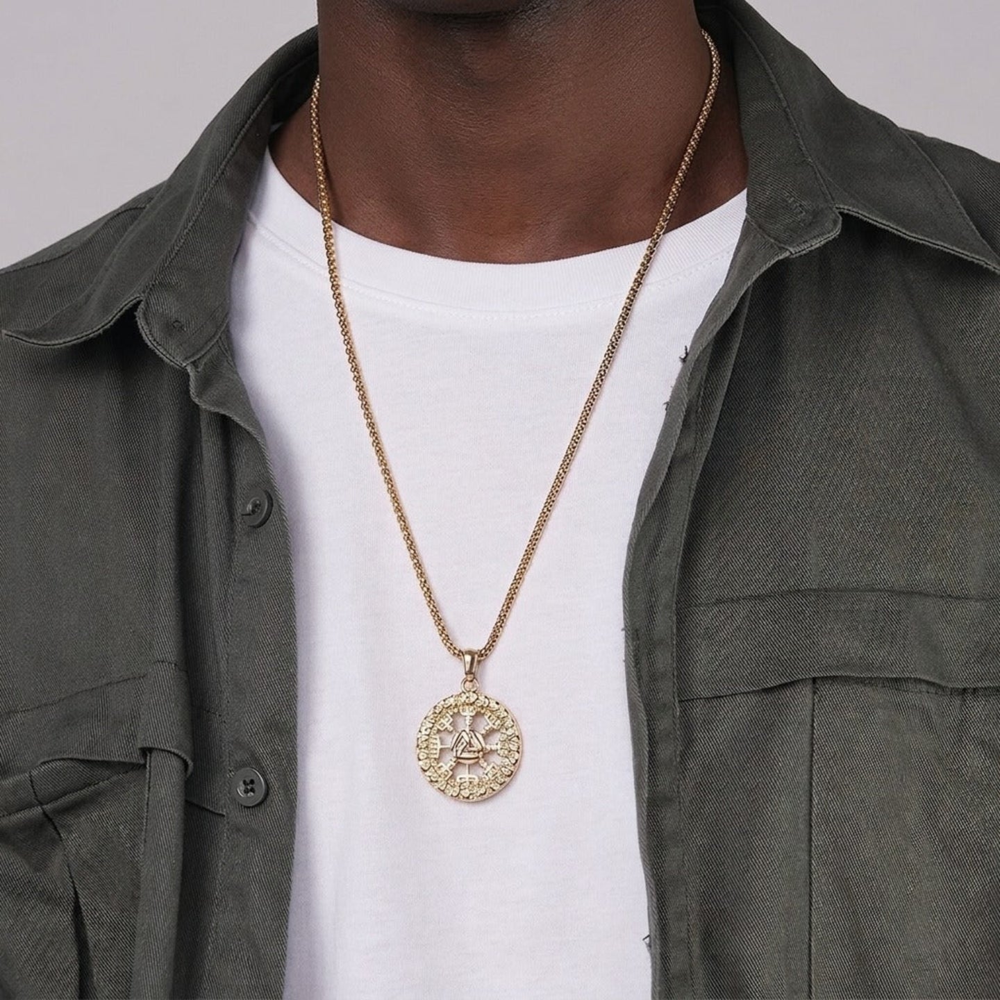 Person wearing a gold necklace with a detailed pendant on a plain background