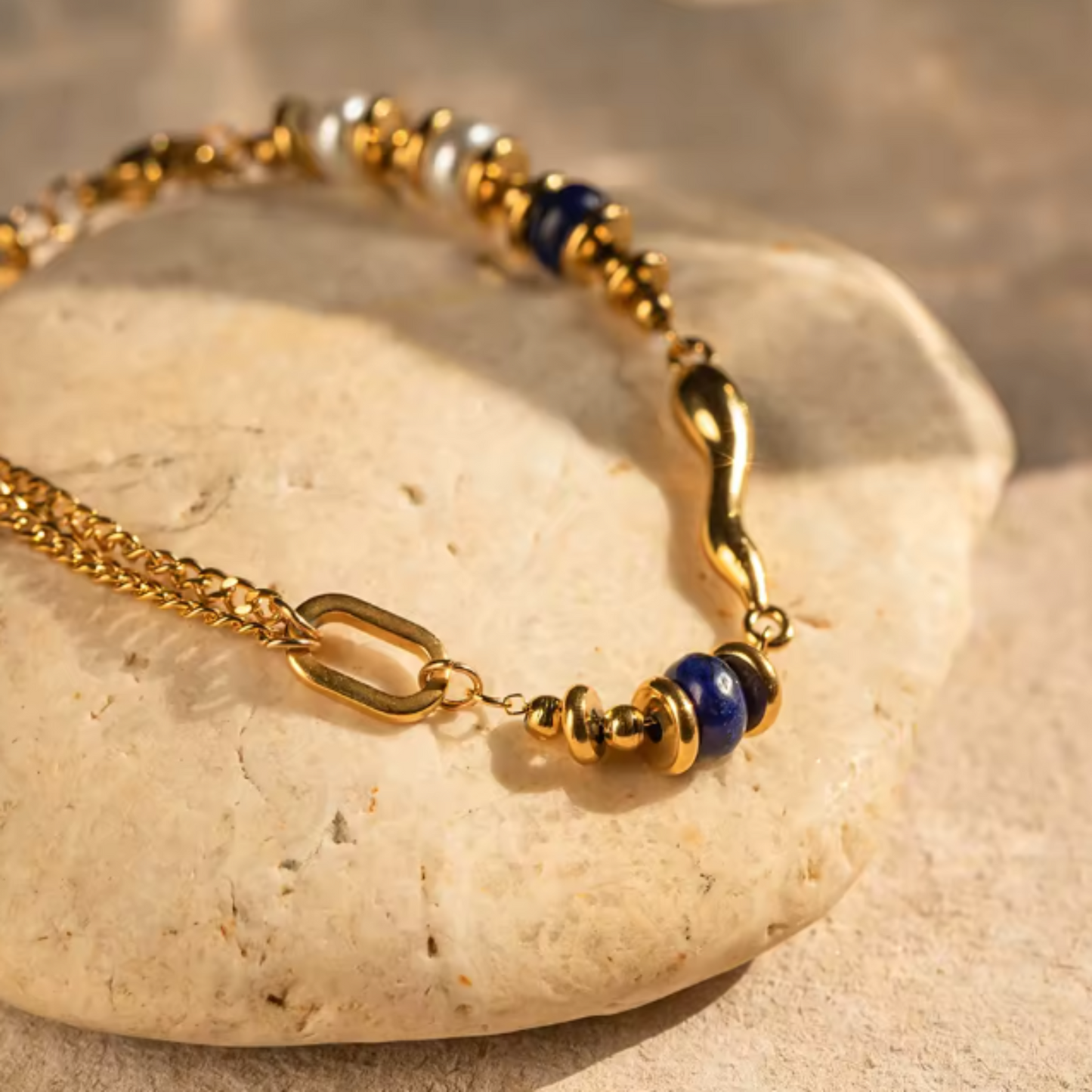 Gold bracelet with blue beads on a stone surface