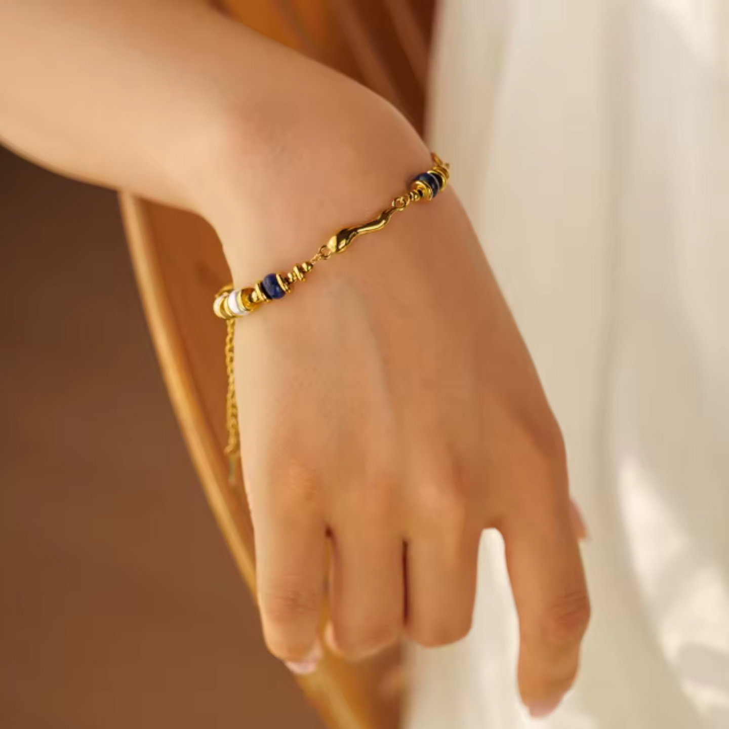 Gold bracelet with blue beads on a wrist against a neutral background