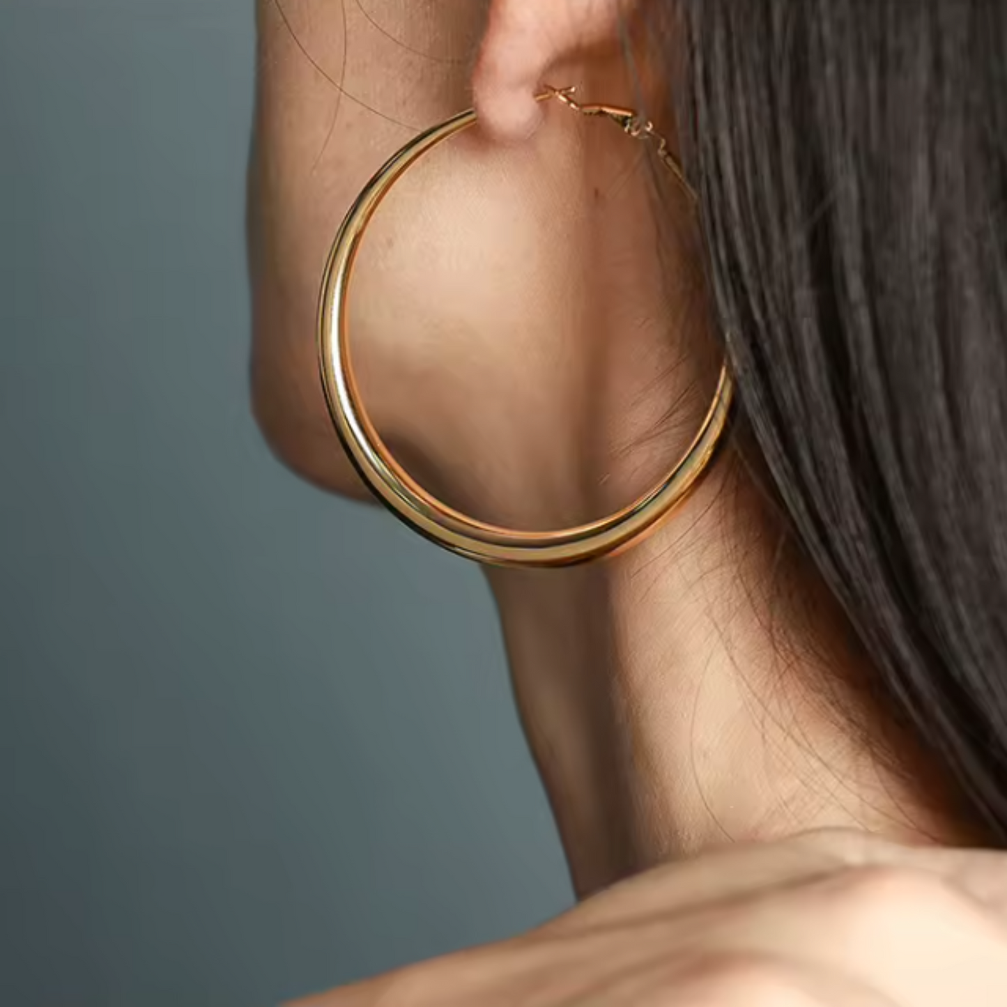 Gold hoop earring worn by a person against a neutral background